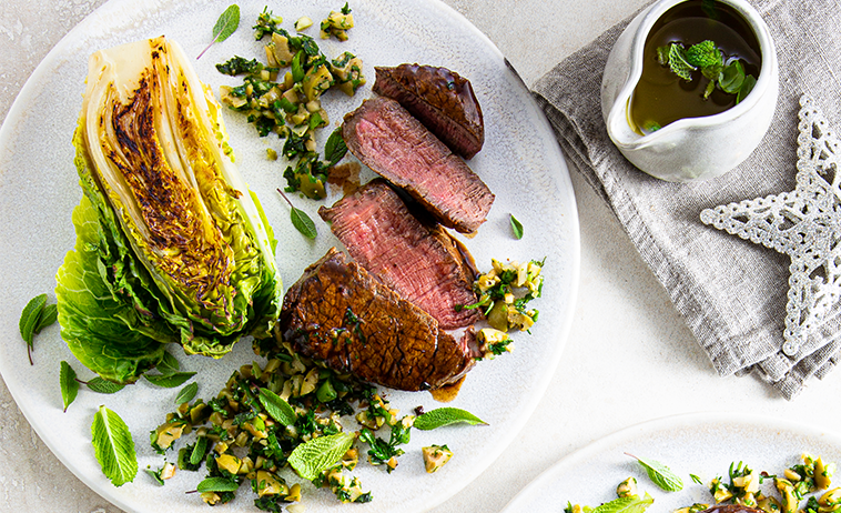 beef eye fillet with green olive tapenade on a white plate