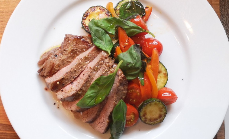 Lamb Rump with Roasted Peppers, Cherry Tomatoes, Courgette & Basil on a white plate