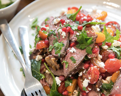 Lamb Medallion, tomato and roasted walnut Salad on a white plate with cutlery on the side