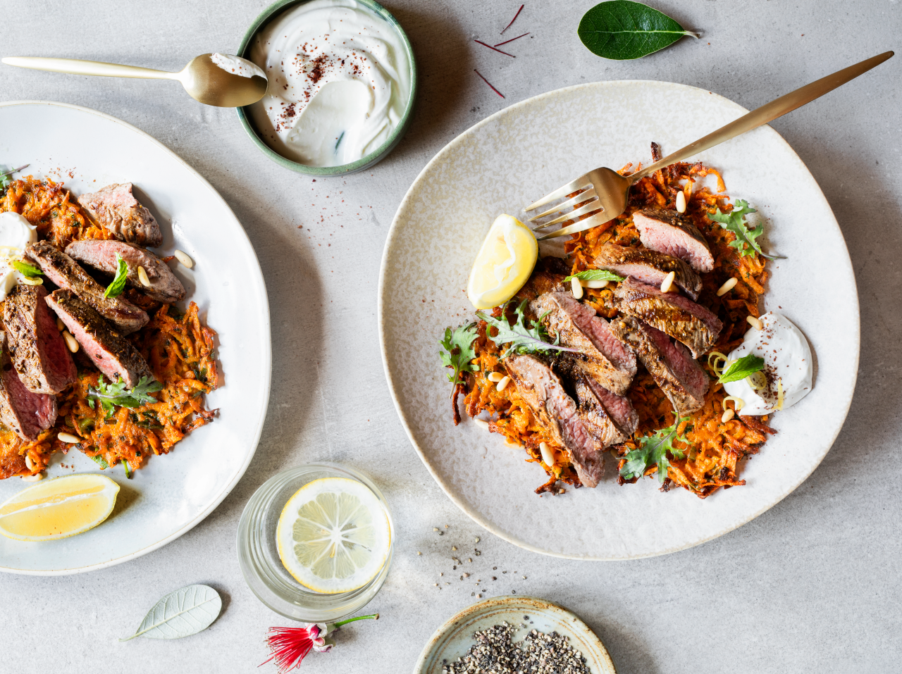 Seared Venison Steaks on Kumara Fritters with Tahini Yoghurt Dressing on plate with a fork and a lemon wedge