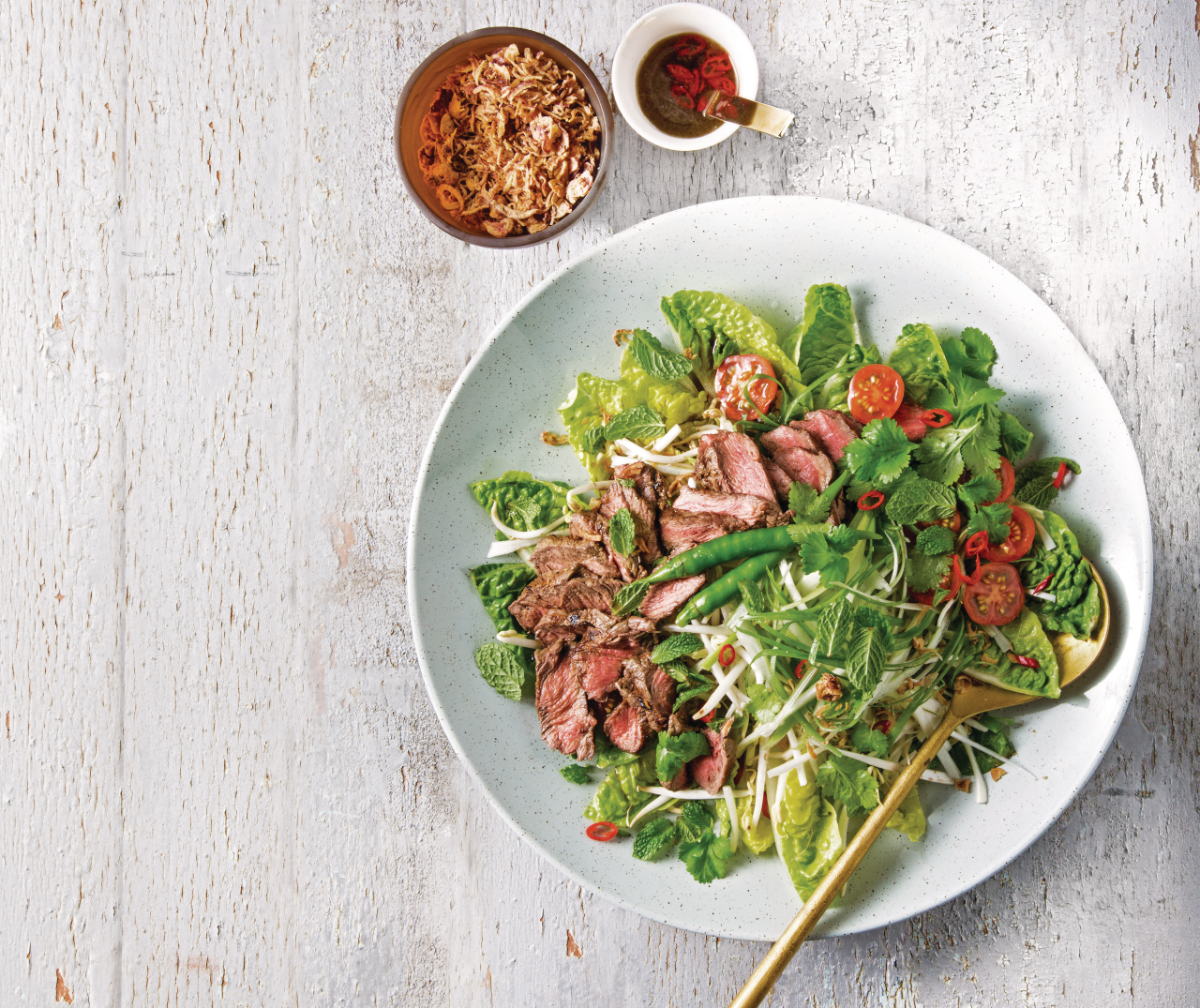 Thai Beef Salad on a white plate with a gold spoon and fried onions on the side