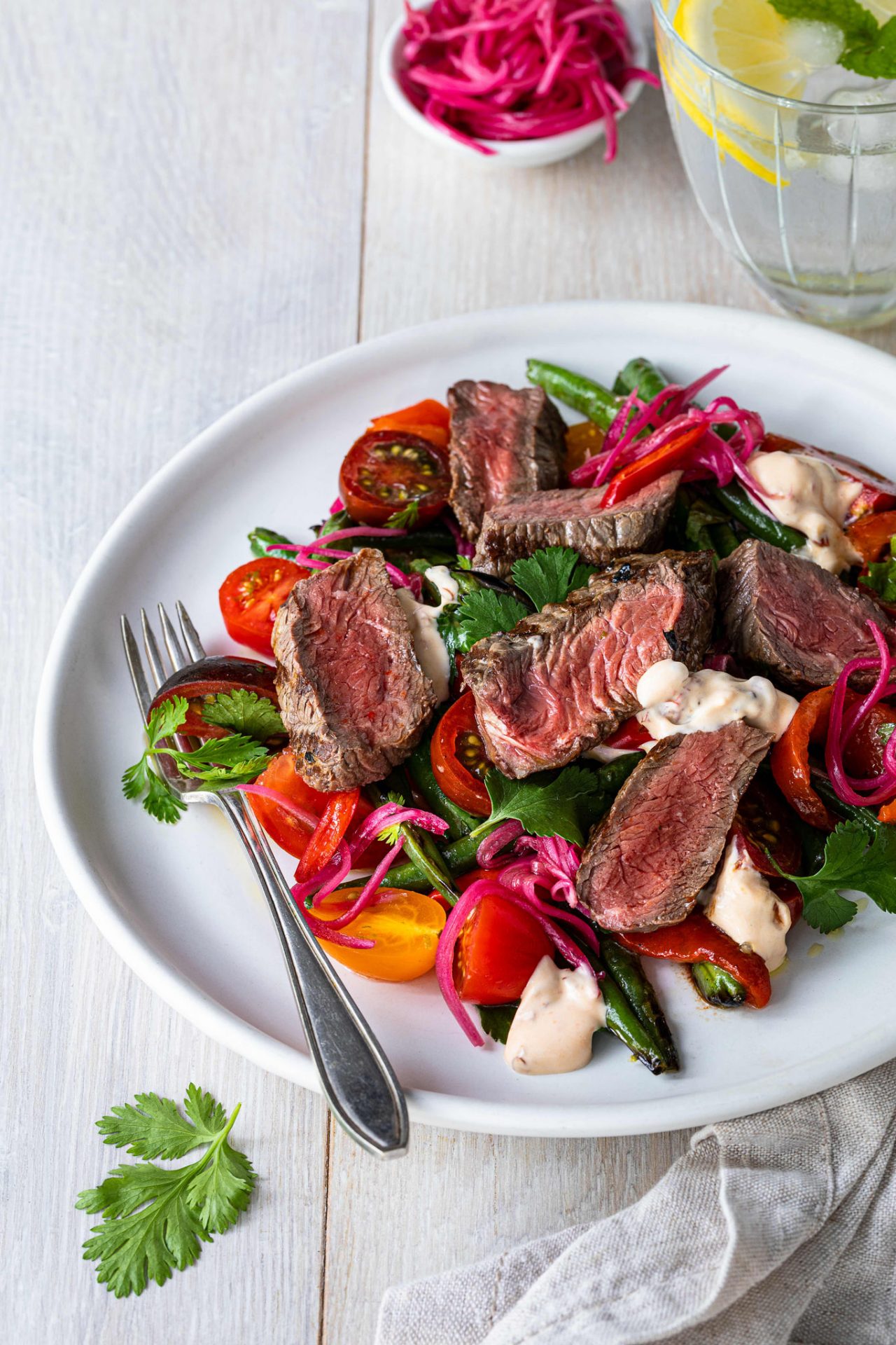 Beef Medallion summer salad with bright tomatoes and mozzarella sits on a white plate with beetroot toppings in background