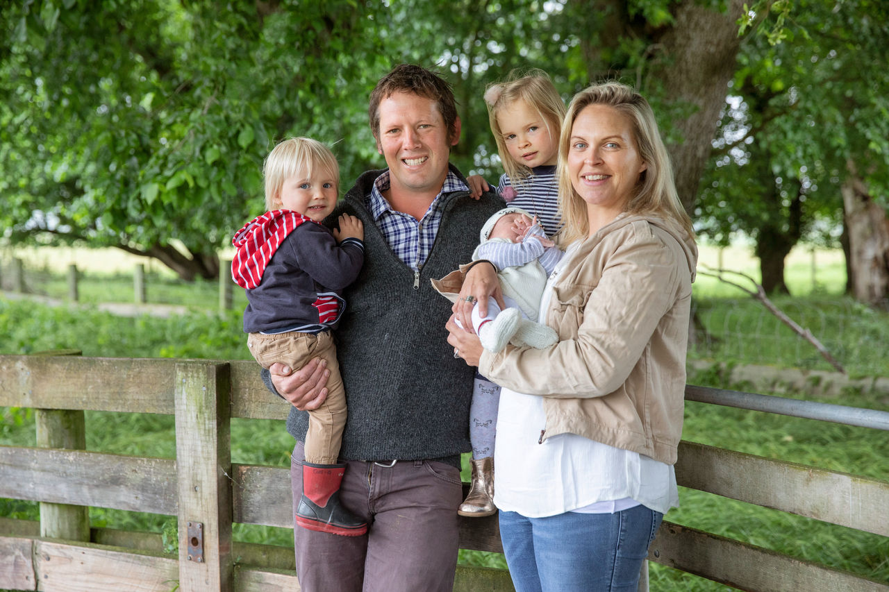 Hamish and Debby Galletly and their three kids standing in front of a wooden fence.