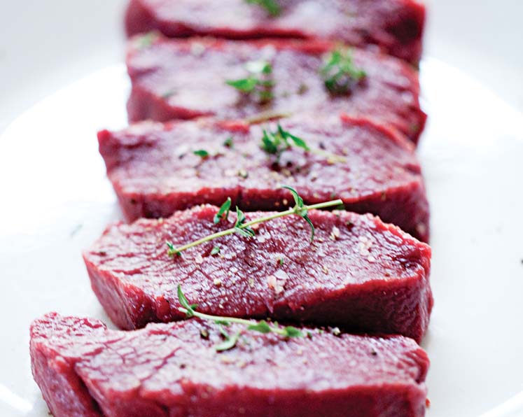 Five pieces of steak with herbs on top sitting on a plate.