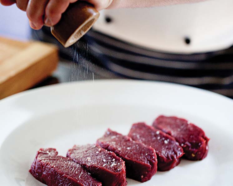 Salt being grinded over 5 pieces of steak