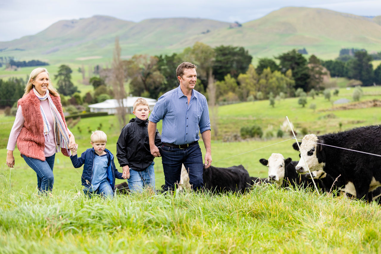 Will and Abbie Foley walking with their two children on their farm with beef cattle pictured beside them.