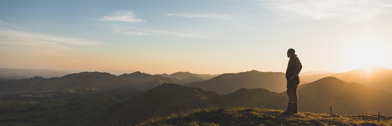A farmer stands on top of a hill looking down on the landscape beneath him