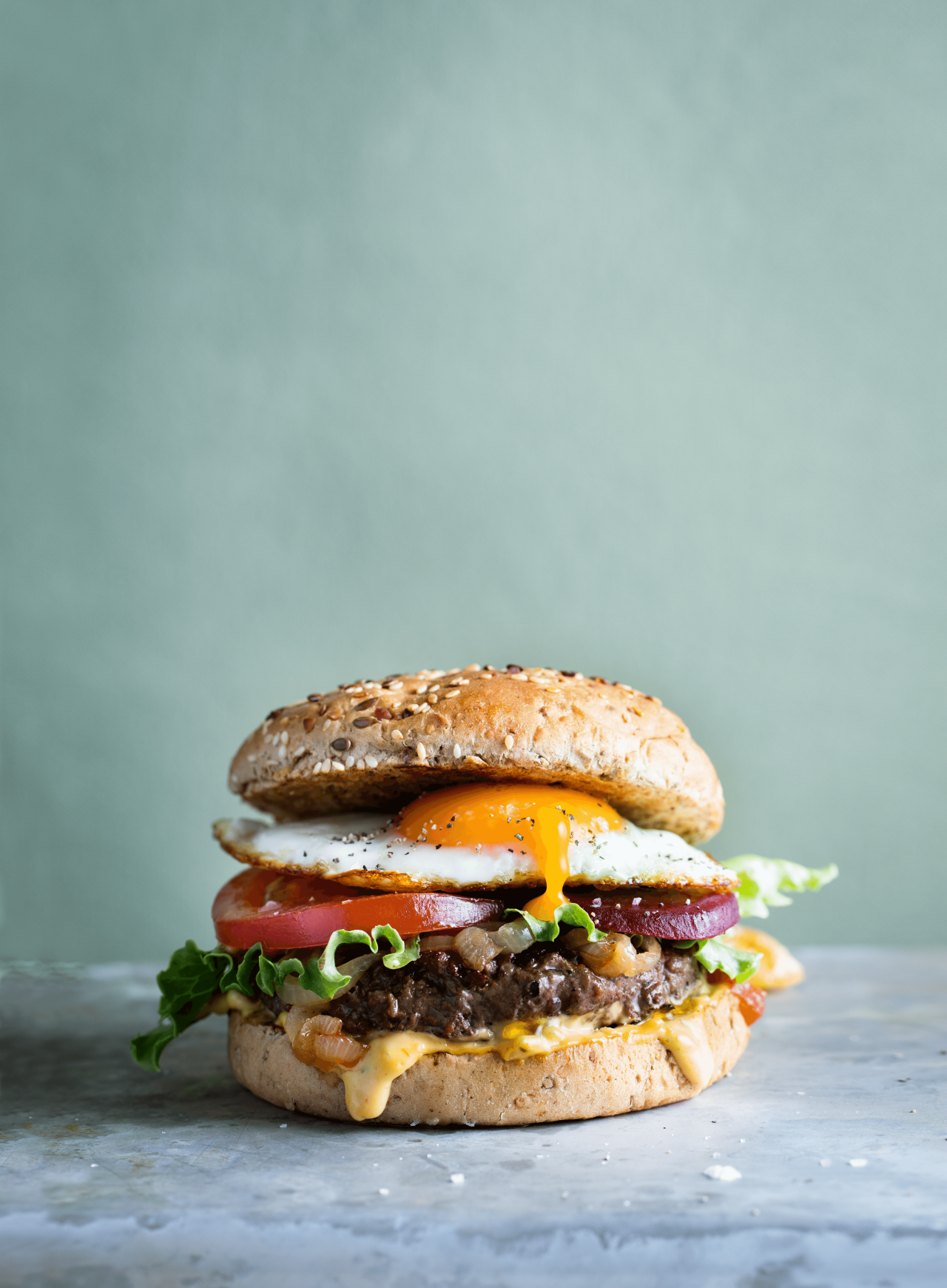 Beef burger with egg, tomato and lettuce sits on a counter.
