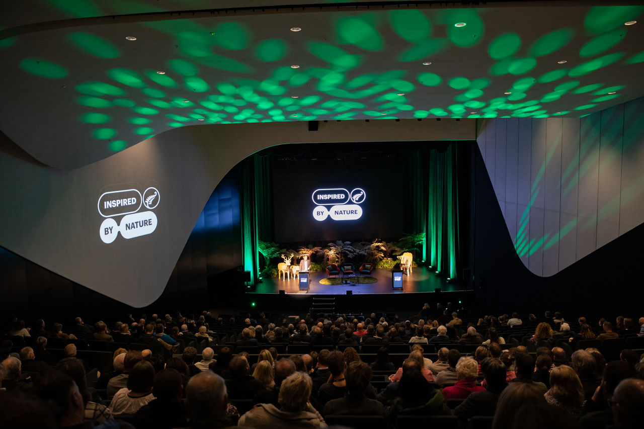 The auditorium at Te Pae Convention Centre, full of attendees at the 2022 Farmer Conference. They are watching the stage where a presentation is occurring. 
