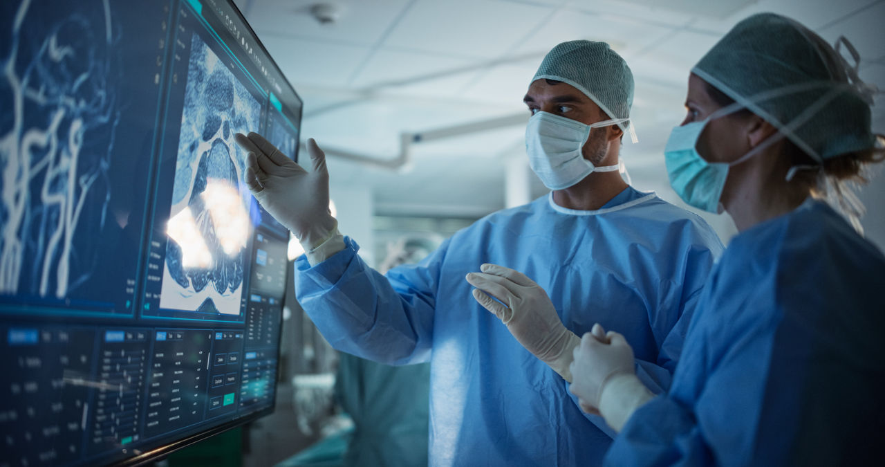 Portrait of a Young Female and Male Surgeons Reviewing Patient's Scans on a Large Screen in a Dimly Lit Operating Room. Their Team of Assistants and Nurses Preparing for a Life-Saving Procedure