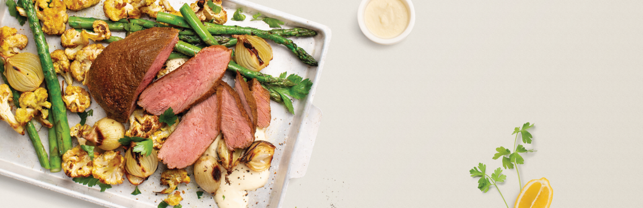 a venison roast dish on a white plate with potatoes next to sauce and a lemon wedge