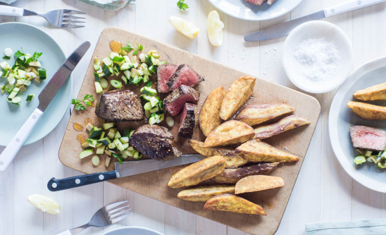 Beef Medallions with Zucchini & Olive Salad and Spiced Kumara Wedges on a chopping board