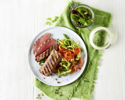 Grilled Lamb Steaks with Sesame Zoodles and Summer Salad on a white plate