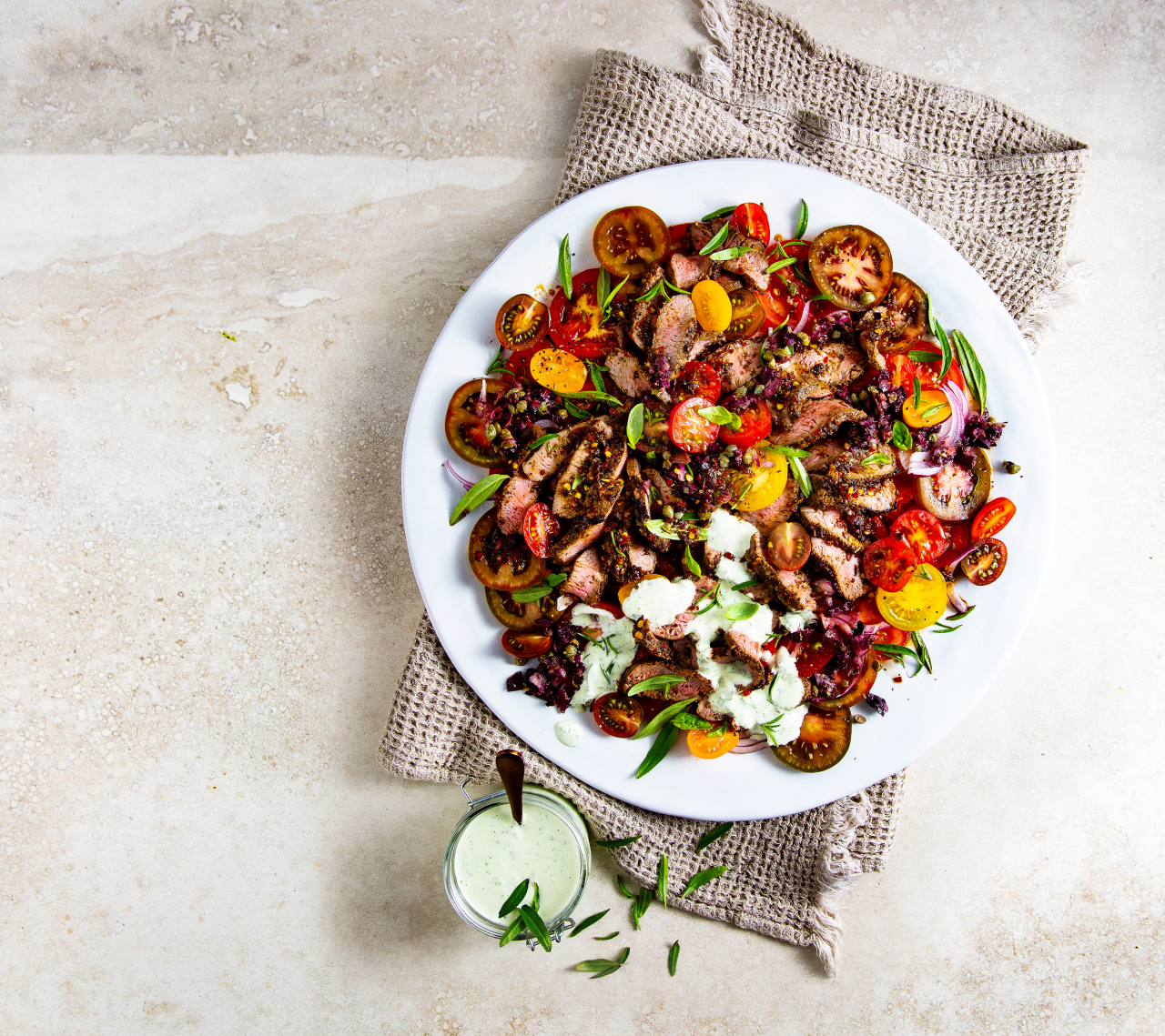 Mediterranean Lamb Loin Salad on a white plate and a cream waffle textured tea towel on