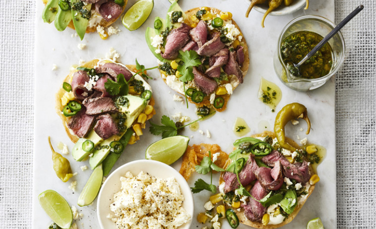 Tostadas with Beef Flat-Iron Steaks on a chopping board next to limes and pesto