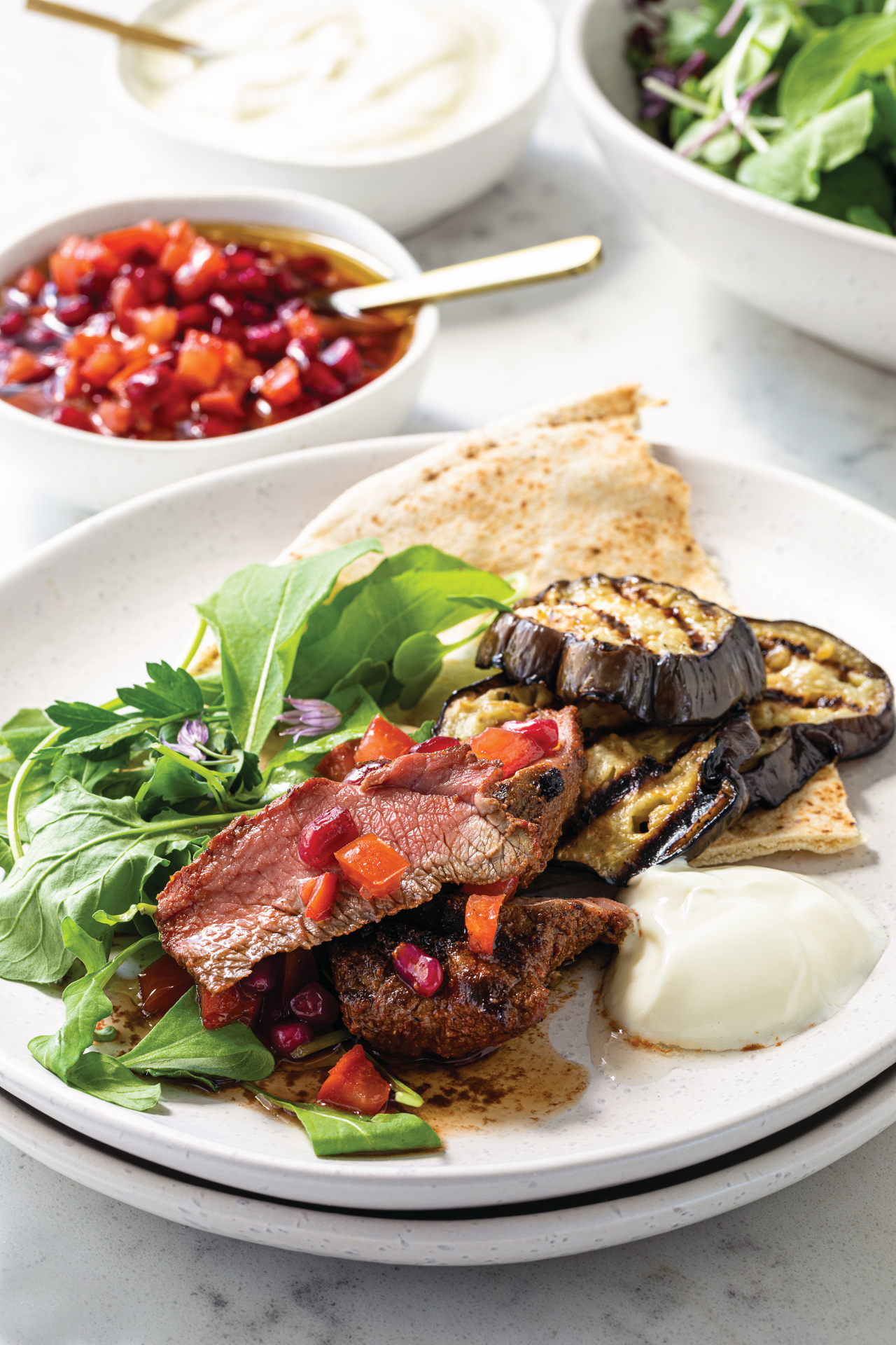 Venison Medallions Flatbreads with Tomato Pomegranate Dressing and Grilled Eggplant on a white plate