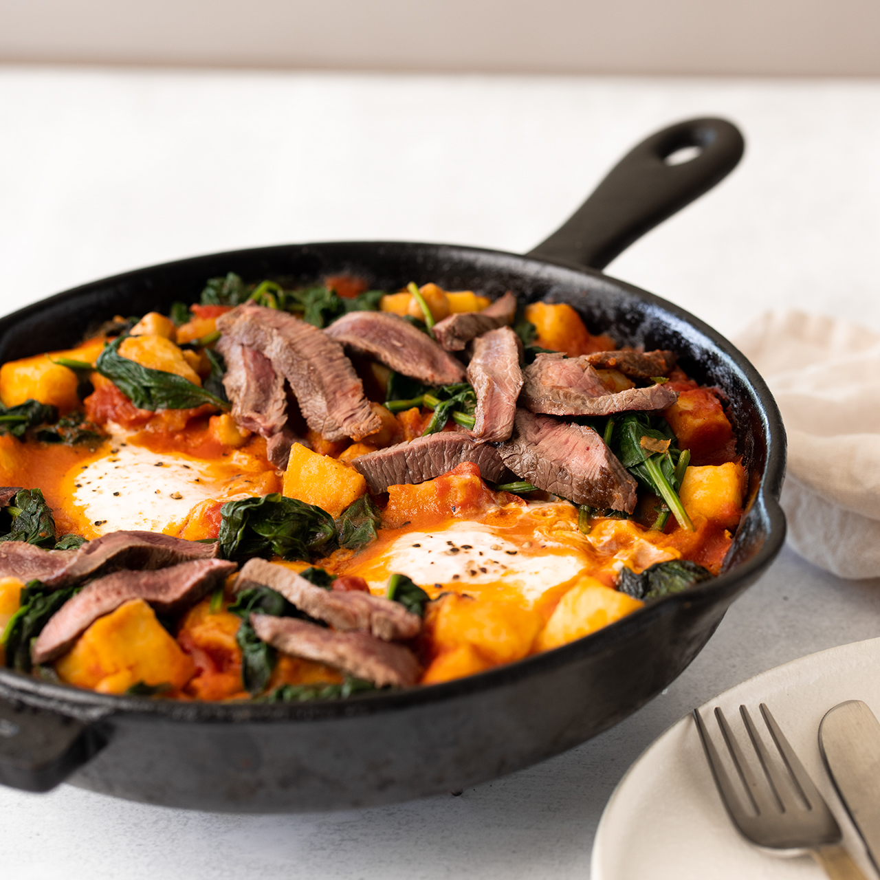 Venison Minute Steak and Egg Hash in a black skillet being served on a table