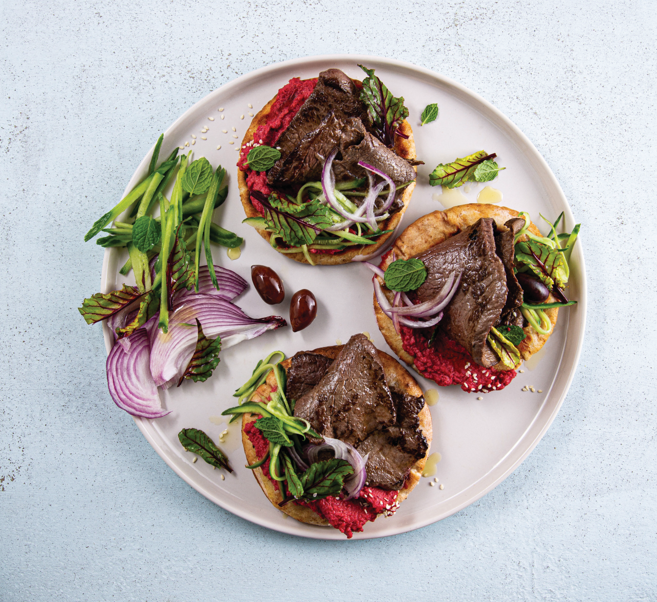 Venison Minute Steaks with Beetroot Hummus on Pita Breads on a cream plate