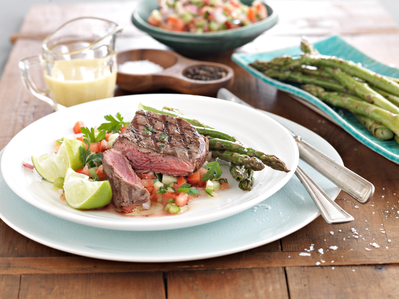 Venison Steak with Creosa Salad and Grilled Asparagus on a plate with wedges of lime on the side of the plate