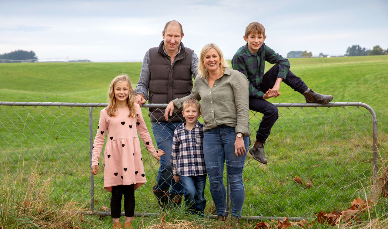 Farmer Story: Ross and Jo Hay with three children leaning against the farm gate with grass in the background