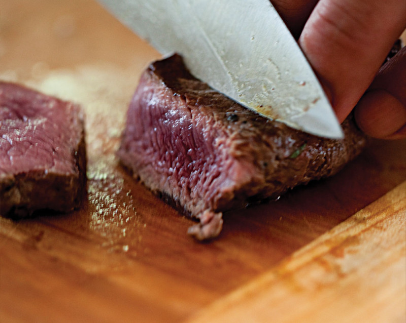 A close up of a lamb cut being sliced on a wooden chopping board